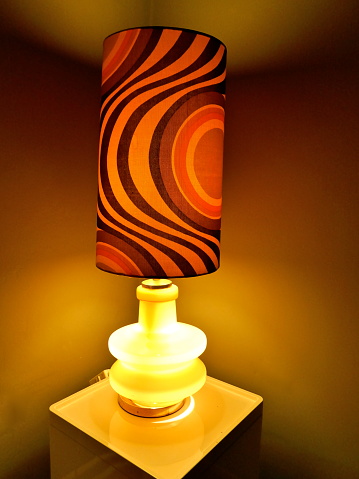 Ambtenaren Nieuwsgierigheid Smederij Table Lamp From The 70s With Orangebrownwhite Patterned Lampshade And A  Lighted Glass Base Stands On A Small Table In The Living Room And Spreads  Warm Cozy Light Stock Photo - Download
