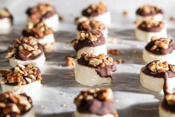 Banana slices covered with chocolate and nuts Frozen banana slices topped with dark chocolate and pecans sitting on a tray covered in wax paper Chocolate Dipped stock pictures, royalty-free photos & images