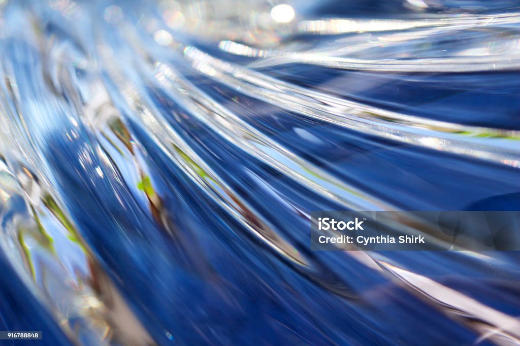 Close up of beautiful wavy surfaced lead crystal glass reflecting bright blue color This macro abstract features the surface of beautiful wavy smooth surfaced lead crystal glass reflecting vibrant blue color in natural light. Crystal Stock Photo