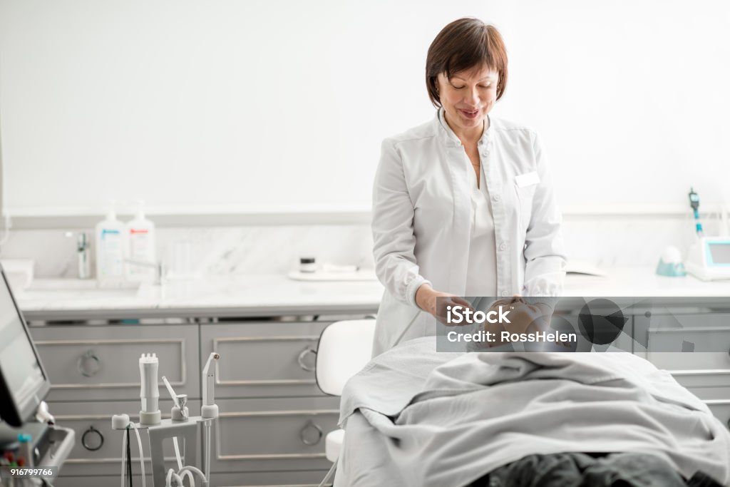 Senior woman cosmetologist during the procedure Senior woman cosmetologist making facial procedure to a young client in a luxury medical resort office Dermatology Stock Photo