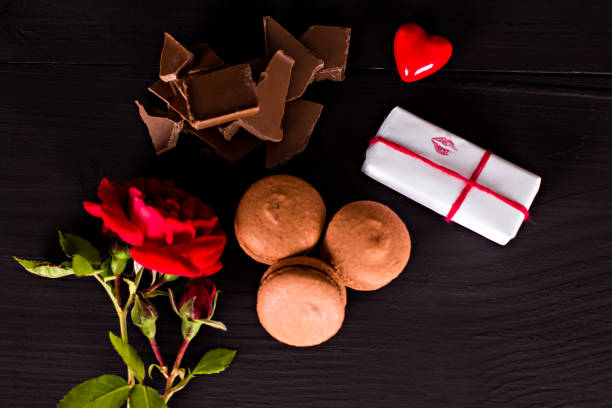 istock Chocolate macaroons, gift and rose flower on a dark background. 916804092