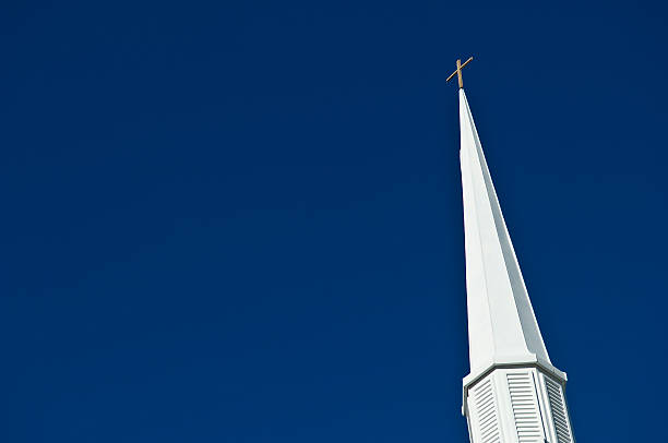 this picture is of a church steeple in the sky. and there is a cross on top of the church steeple. the church steeple is white and on top of a local church. the sky is clear blue. and the picture was taken during the day. and the sunlight is natural sunlight. 