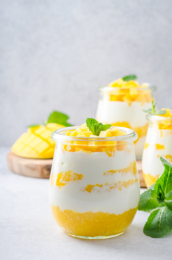 Three glass jars with greek yogurt and mango on a light table. Copy space, vertical image, front view