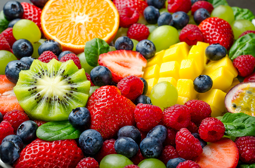 Fruit platter with various fresh strawberry, raspberry, blueberry, tangerine, grape, mango, spinach. Close-up, horizontal image