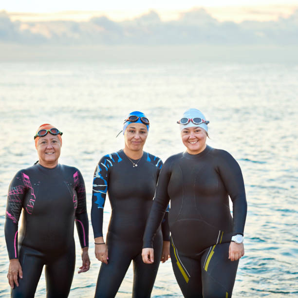 istock Smiling female friends in wetsuits at beach 916830340