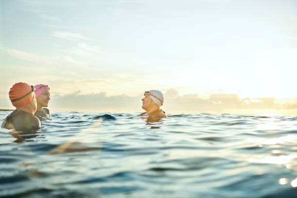 women talking while swimming in sea during sunset - group of people women beach community imagens e fotografias de stock