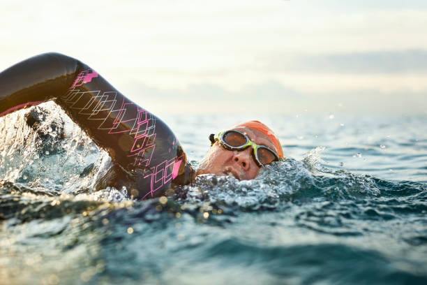 determinata donna matura che nuota in mare - competitive sport competition swimming wetsuit foto e immagini stock