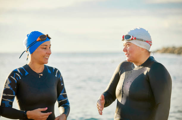 istock Mature friends in wetsuit talking at beach 916830566