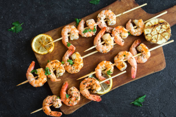Grilled shrimp skewers Grilled shrimp skewers. Seafood, shelfish. Shrimps Prawns skewers with herbs, garlic and lemon on black stone background, copy space. Shrimps prawns brochette kebab. Barbecue srimps prawns. prawn grilled seafood prepared shrimp stock pictures, royalty-free photos & images