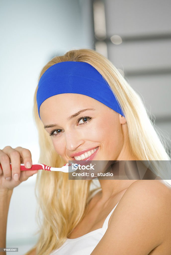 Młoda szczęśliwa kobieta czyszczenia zębów szczoteczki do zębów w łazience - Zbiór zdjęć royalty-free (Blond włosy)