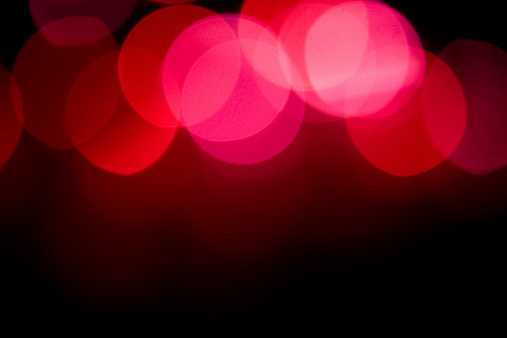 Red and pink lights defocused for a colorful abstract effect are placed at the top half of the image with softer blurred transition below it, fading into a vert dark background.