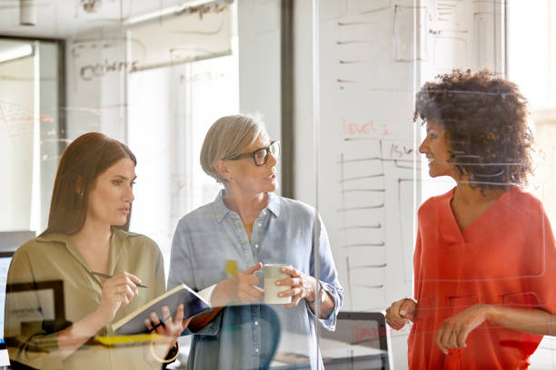 istock Businesswomen discussing plan at glass wall 916844666