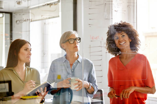 istock Businesswomen looking at plan on glass wall 916844692