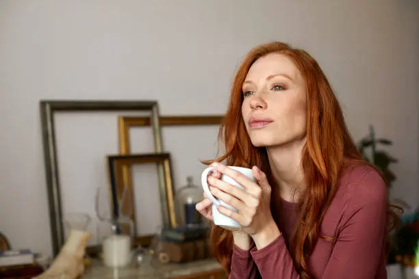 Photo of Thoughtful woman having coffee from mug at home