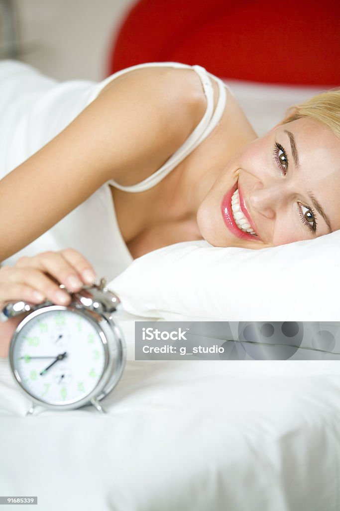 Молодая женщина с alarmclock на кровати на утро - Стоковые фото Благополучие роялти-фри
