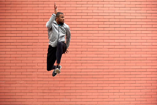 Determined athlete jumping in mid-air. Full length of young male exercising against wall. He is in sportswear.