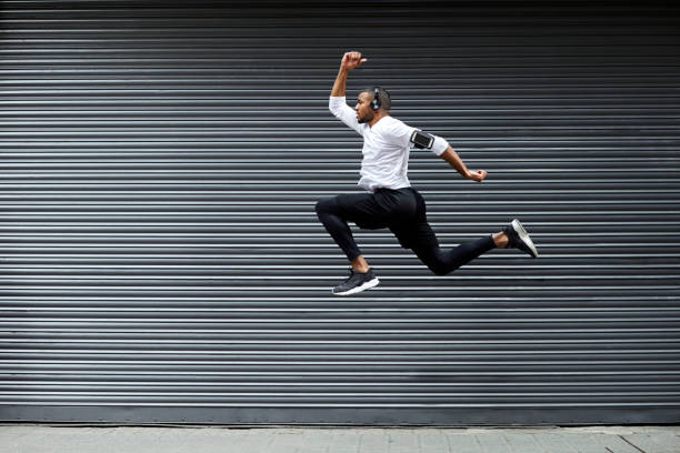 Sporty young man jumping against shutter Full length of determined young man jumping against shutter. Side view of fit male jogger is exercising in mid-air. He is wearing sports clothing. running motion stock pictures, royalty-free photos & images