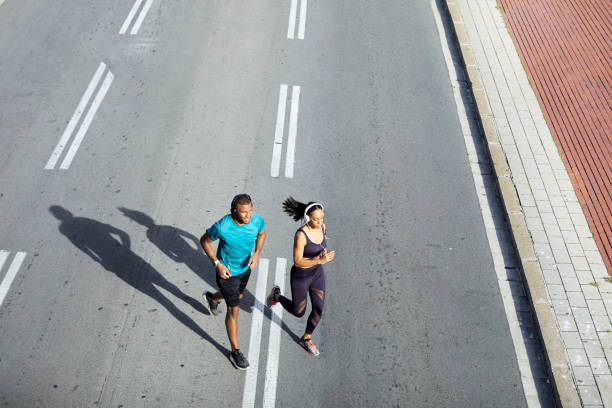 Couple jogging on city street during sunny day"n Couple jogging on city street. High angle view of man and woman running together. They are in sports clothing on sunny day."n forward athlete stock pictures, royalty-free photos & images