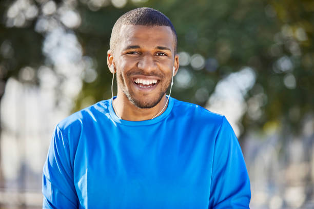 Portrait of happy man with headphones at park Portrait of happy man wearing headphones. Smiling young male is listening music at park. He is in blue t-shirt. blue t shirt stock pictures, royalty-free photos & images