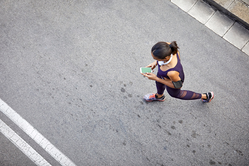 High angle view of woman using mobile phone. Young female is walking on street. She is in sports clothing.