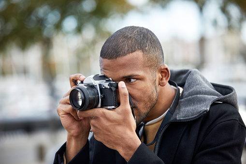 Close-up of young man photographing through camera. Male is wearing jacket. He is holding old-fashioned equipment.