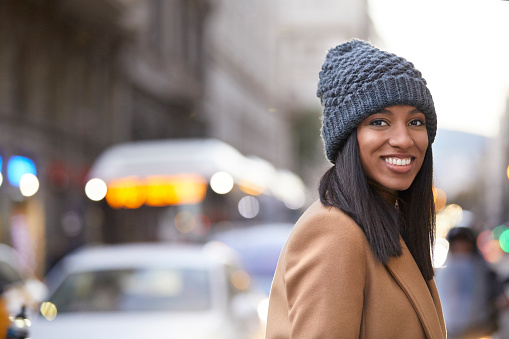 Portrait of smiling young woman wearing knit hat. Beautiful female is standing on city street. Tourist is enjoying her vacation.