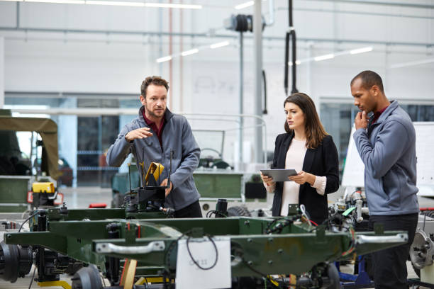 Engineer discussing with colleagues in car factory Automobile engineer showing incomplete car while discussing with colleagues. Multi-ethnic male and female professionals are standing at car production line. They are in automotive industry. car plant stock pictures, royalty-free photos & images