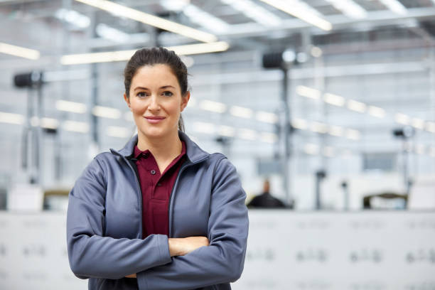 Female engineer with arms crossed in car plant Portrait of female engineer with arms crossed in automobile industry. Confident technologist is standing in showroom. She is in jacket at factory. production line worker stock pictures, royalty-free photos & images