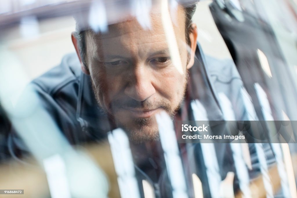 Engineer seen through car windshield in industry Close-up of male engineer seen through car windshield. Confident male is repairing vintage vehicle in automobile industry. Technologist is smiling while working in showroom. Car Stock Photo