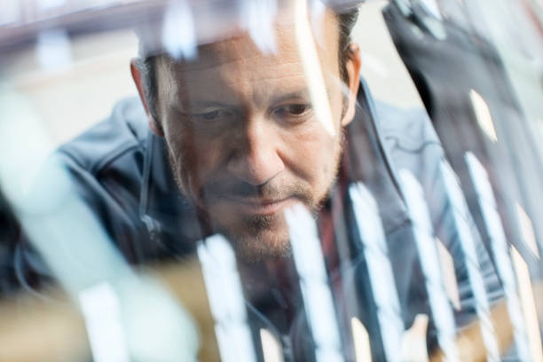 Engineer seen through car windshield in industry Close-up of male engineer seen through car windshield. Confident male is repairing vintage vehicle in automobile industry. Technologist is smiling while working in showroom. car plant photos stock pictures, royalty-free photos & images