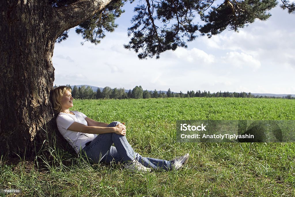 Joven belleza mujer sentarse bajo solo árbol en campo - Foto de stock de Adulto libre de derechos