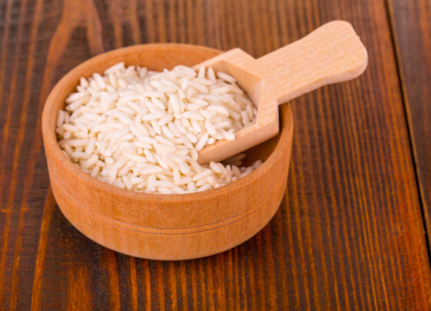 istock raw white rice in a Cup with wooden spoon on a wooden table. 916873662