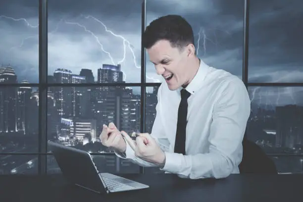Angry caucasian businessman working on laptop, showing his middle finger to something annoying on the screen