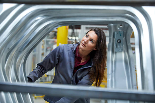 Female maintenance engineer examining car chassis Maintenance engineer examining car chassis. Confident professional is looking at body of vehicle in factory. Female expert is manufacturing in automobile industry. production line automobile industry car plant car stock pictures, royalty-free photos & images