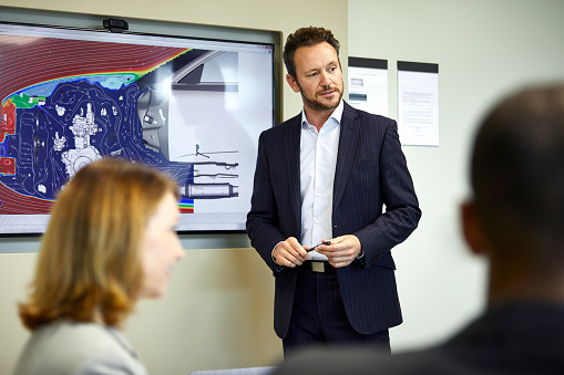 Businessman discussing with colleagues while giving presentation. Male executive is wearing formals. They are in office meeting .