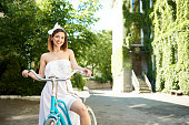 Horizontal portrait of a happy beautiful young woman in a white dress sitting on a bicycle smiling to the camera joyfully copyspace smile toothy happiness enjoyment recreation freedom youth.