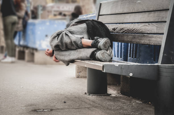 Poor homeless man or refugee sleeping on the wooden bench on the urban street in the city, social documentary concept, selective focus Poor homeless man or refugee sleeping on the wooden bench on the urban street in the city, social documentary concept, selective focus homelessness stock pictures, royalty-free photos & images