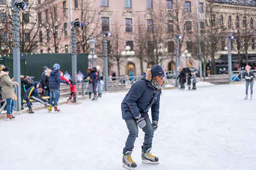 Stockholm, Sweden - February 03, 2018: Front view of a young man skating at a public ice skating rink outdoors in the city center of Stockholm february 03, 2018. Incidental people in the background.
