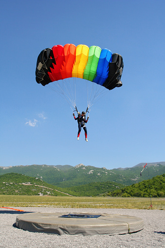 A paraglider flying in the blue sky with mountain in background.
