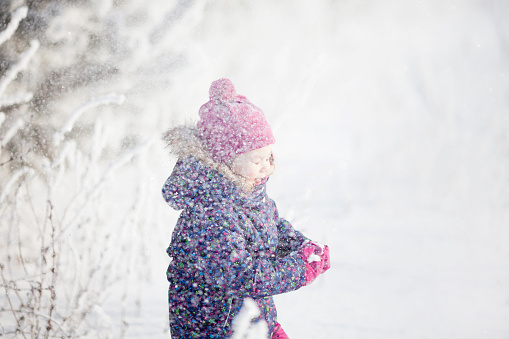 Cute toddler girl outdoors on a sunny winter day, having fun, playing snowballs, snowy day.