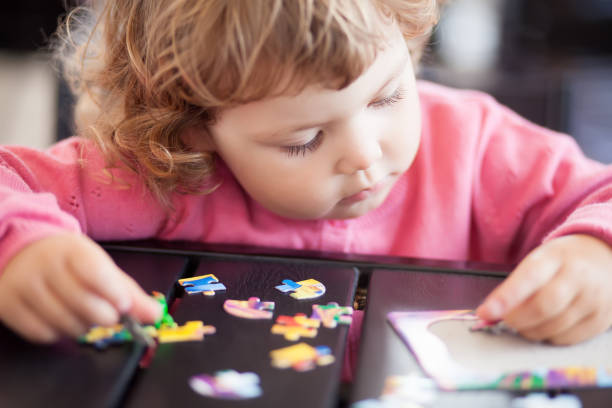 Blonde toddler girl, solving puzzle on a table, having fun. Early education and developement. Little genius concept.