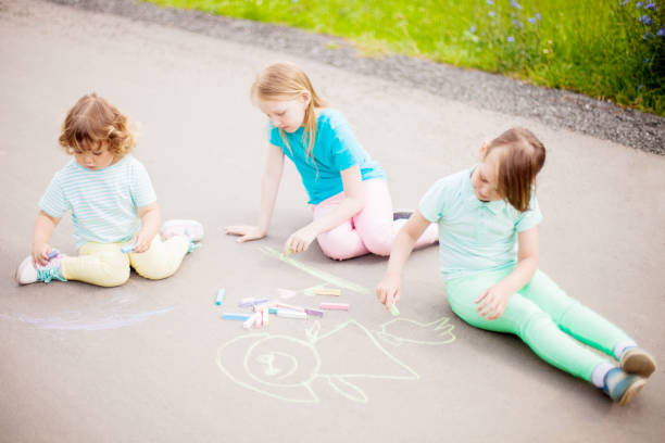 istock Little sisters draw with color chalk outdoors. Chalk drawings. 916914606