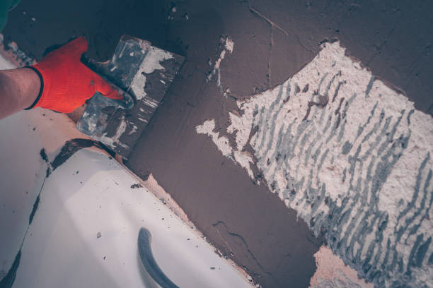 istock Worker level the wall over the bathroom with tile adhesive applying it with a spatula, preparation for tiling 916921822