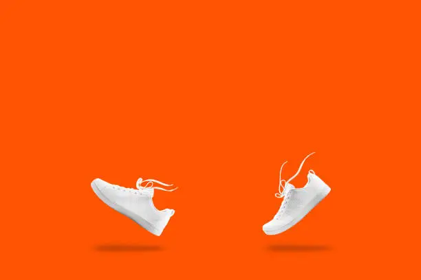 Photo of Pair of White sneaker composition like walking and floating rope isolated on orang  background with clipping path