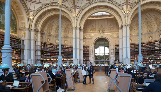 National Library of France, Paris, on the Richelieu site. Students are working on laptops, surrounded by bookshelves, under the 18th century domed roof. The building dates back to the 17th and 18th centuries.
