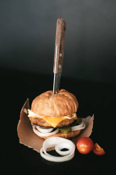 istock Handmade burger with beef, pickles, cheese and knife on black wooden table. 916930846