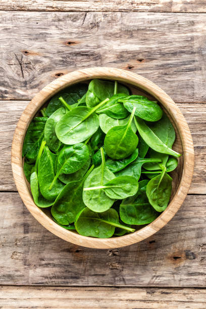 fresh baby spinach leaves in bowl on wooden background - espinafres imagens e fotografias de stock