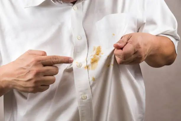 Photo of Person pointing to spilled curry stain on white shirt.