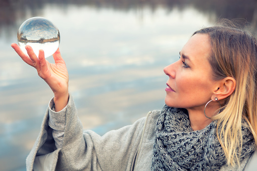 portrait of blond woman in front of lake holding up a glass ball
