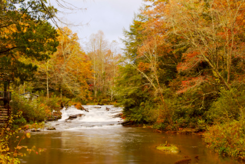 Soque River in Clarkesville Georgia USA shot in the month of October when all the trees were changing colors. The waterfall was shot with a slow shutter speed for a silky smooth effect. There is a log house on the left side of the image tucked away under the trees. 